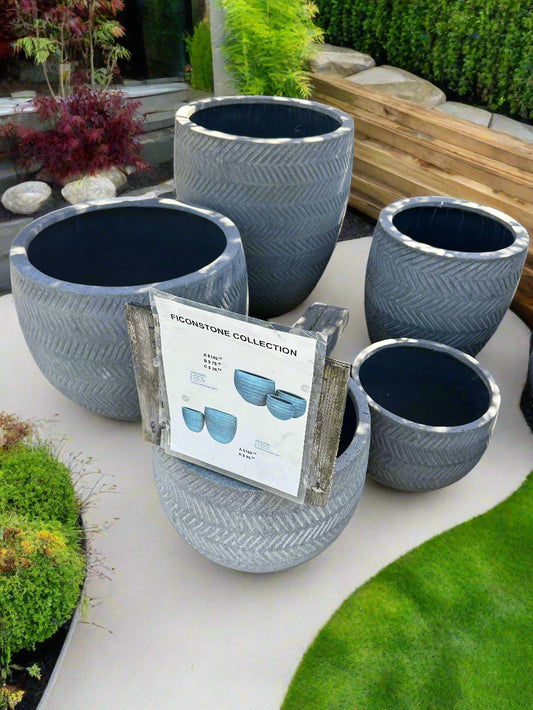Stack of gray concrete planters with a product packaging on top, set against a blurred outdoor background.
